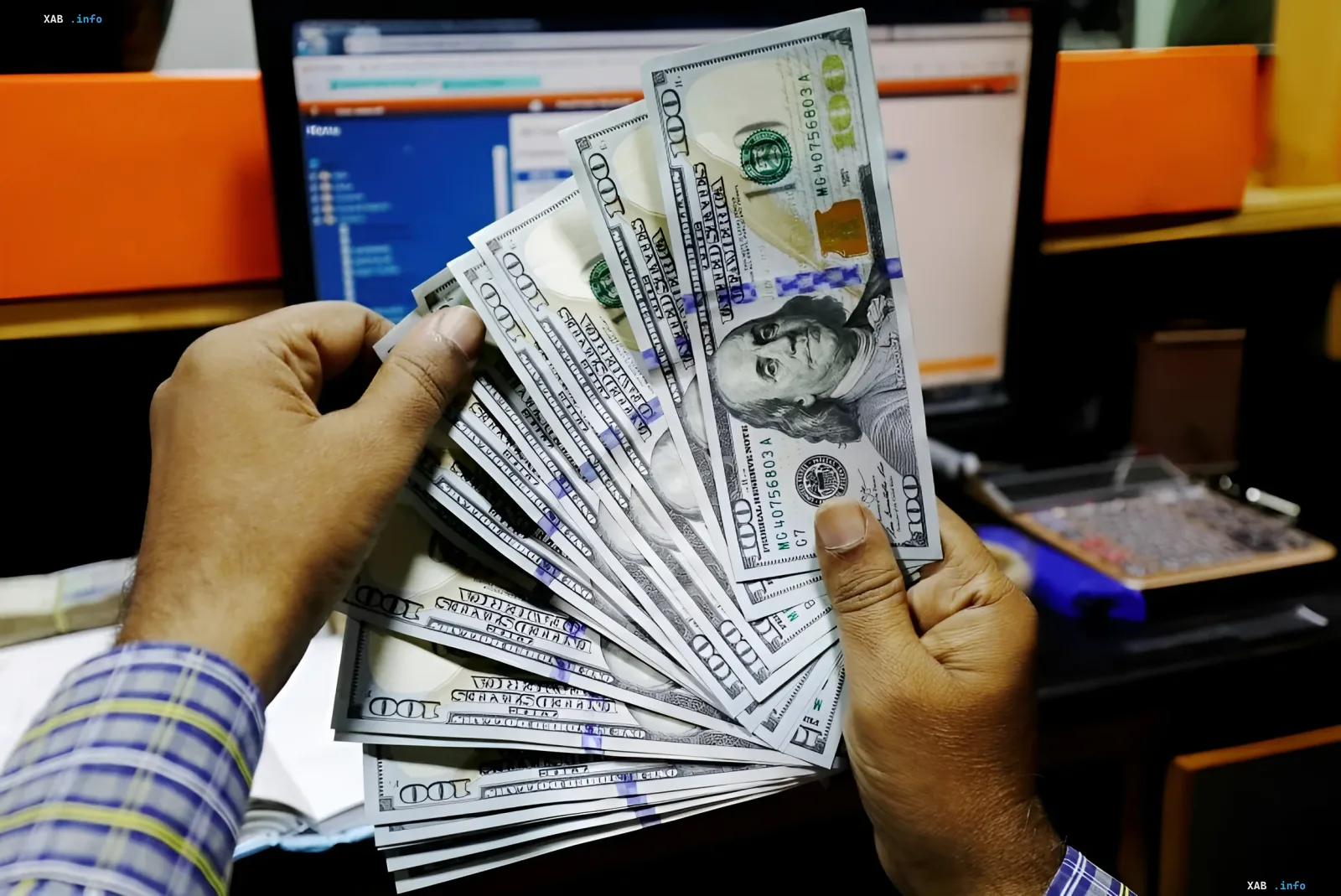 Инсайдеры США распродают акции: руки держат пачку долларовых купюр на фоне монитора с биржевыми данными