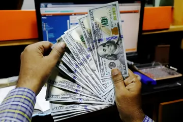 US insiders selling stocks: hands holding a stack of dollar bills against a monitor with stock market data