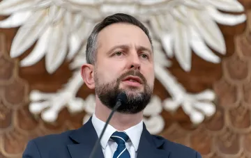 Министр обороны Польши выступает с речью на фоне герба, обсуждая отношения с Украиной и угрозы со стороны Кремля
