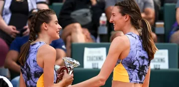 Athletes in blue and yellow outfits hold a trophy and smile at each other at a tennis tournament in London