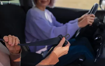 Beifahrer schnallt sich im Auto an, während Fahrer am Steuer sitzt – Illustration zu Artikel über Bußgelder für nicht angeschnallte Beifahrer