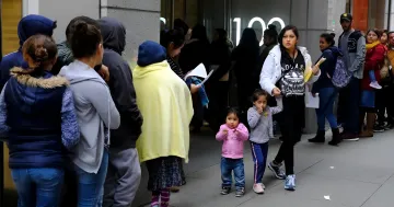 Warteschlange von Einwanderern mit Kindern vor einem USCIS-Gebäude in den USA, die neue Regeln zur öffentlichen Belastung bei Green-Card-Anträgen veranschaulicht