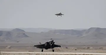 F-35-Jagdflugzeuge auf der Startbahn: ein Flugzeug hebt ab, ein anderes bereitet sich zum Start vor vor einer Wüstenlandschaft