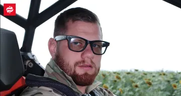 Kommandeur des Bataillons 'Da Vinci Wölfe' in Brille und Tarnuniform, sitzend in einem Fahrzeug vor einem Sonnenblumenfeld, nachdem er eine Verwarnung von Syrsky erhalten hat