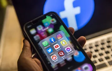 Смартфон с папкой 'Social' и иконками Facebook, Instagram, X (Twitter), YouTube и других соцсетей на фоне логотипа Facebook — иллюстрация глобального сбоя платформ