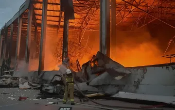 Пожежа в логістичному хабі Київської області після нічної атаки РФ: пожежник гасить вогонь серед згорілих автомобілів та зруйнованої конструкції будівлі