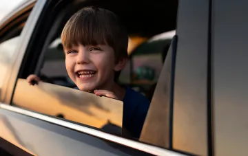 Happy child looking out of car window — illustration for article on child transport rules in Ukraine