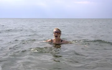 Женщина в очках с открытым ртом в холодной воде, демонстрируя реакцию организма на температурный контраст