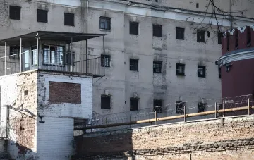 Тюрьма в России: стены с колючей проволокой и barred окна, где содержатся заключенные, включая наркоторговцев и воров атомных бомб, готовых к отправке на фронт