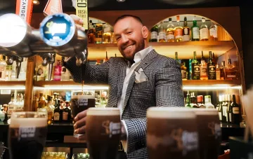 Conor McGregor behind the bar, pouring beer and smiling, demanding a trilogy with Holloway