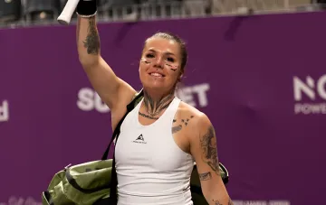 Ukrainian tennis player Marta Kostyuk holding a racket and bag against a purple tournament banner, symbolizing the success of Ukrainian athletes in Hamburg
