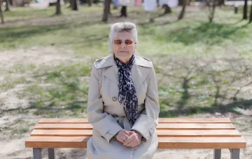 Rentnerin mit Sonnenbrille sitzt auf einer Parkbank, symbolisiert das Renteneintrittsalter und die Notwendigkeit, fehlende Arbeitsjahre in der Ukraine nachzukaufen
