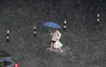 Woman with umbrella and bags walking through deep water in Ternopil or Khmelnytskyi during flooding