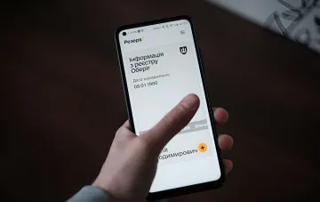 Человек просматривает приложение Резерв+ на смартфоне, где отображается информация из реестра Оберіг с датой рождения — символ цифровизации процесса переоформления отсрочки от мобилизации в Украине