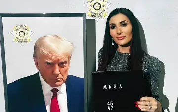Laura Loomer mit MAGA-Schild neben Donald Trump-Porträt in einer simulierten Verhaftungsszene