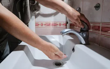 Person dreht Wasserhahn über Waschbecken ein — Symbol für die Absage des steilen Wasserpreis-Anstiegs in Kiew