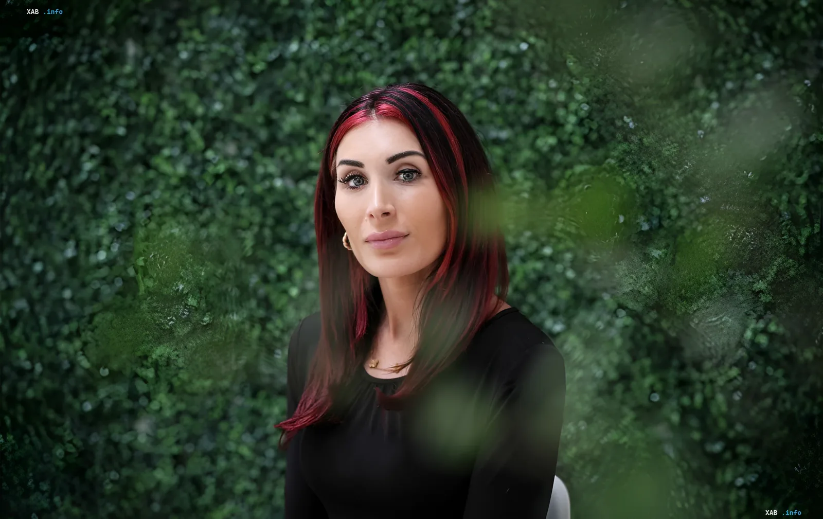 Laura Lumer mit roten Haaren vor einem Hintergrund aus grünem Laub, was ihre persönliche Erfahrung in der Ukraine symbolisiert