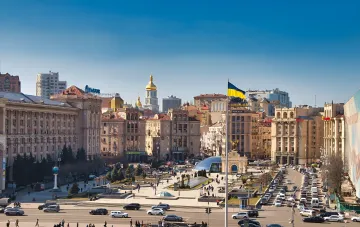 Панорама Майдана Незалежности в Киеве с украинским флагом и золотыми куполами, символизирующая центр города, где меняются правила выбора жилья из-за войны