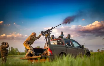 Украинский солдат в камуфляже стреляет из крупнокалиберного пулемета, установленного на пикапе, на фоне заката — иллюстрация к статье о новых правилах для контрактников ВСУ