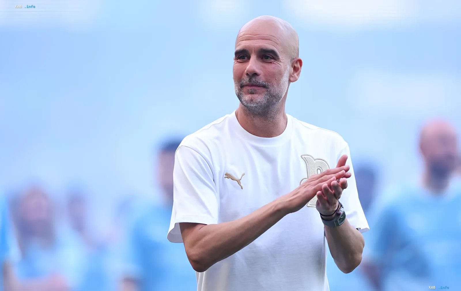 Pep Guardiola in weißem Puma-T-Shirt mit goldenem Logo, klatscht vor verschwommenem Stadionhintergrund – Moment nach Ablehnung des Angebots der italienischen Nationalmannschaft