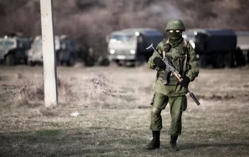 Український військовий з автоматом на фоні військової техніки в Сумській області