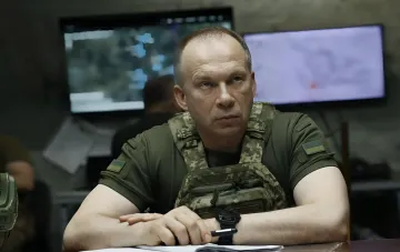 Александр Сырский в военной форме за столом с мониторами на фоне, символизирующий его роль в командовании ВСУ перед сменой власти
