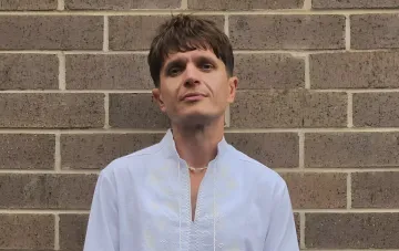 Host Anatolich in white embroidered shirt against brick wall — photo after car accident in Kyiv