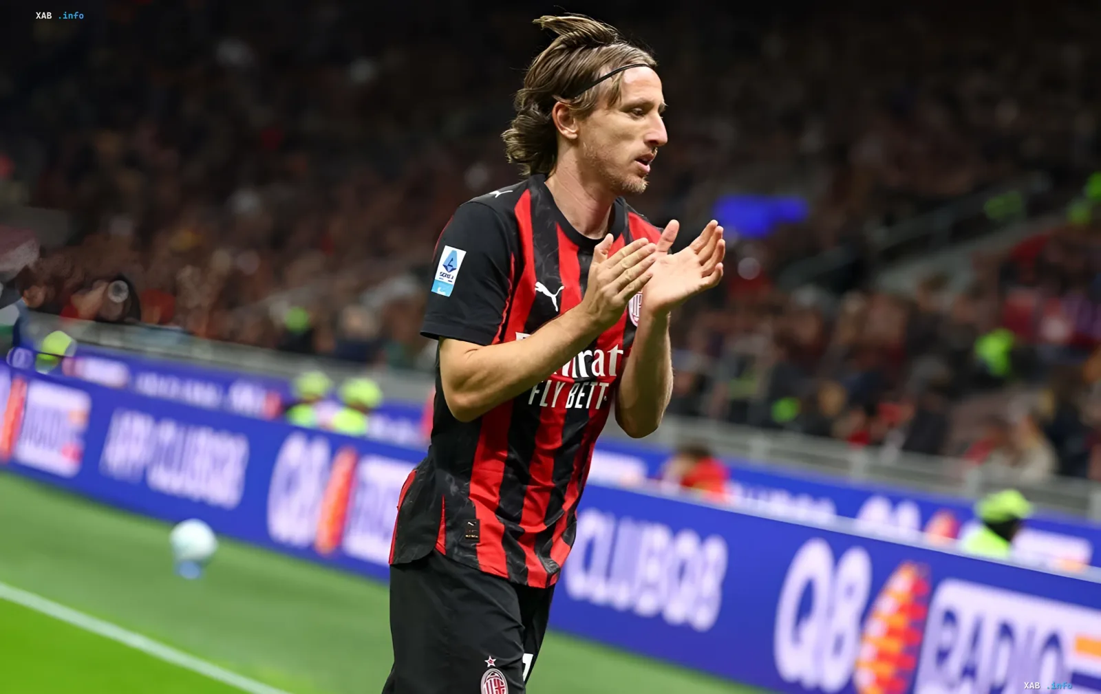 Luka Modric in AC Milan's red-and-black kit applauding on the pitch, set to extend his contract at age 41
