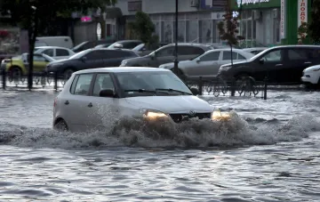 Белый автомобиль Skoda пробирается сквозь глубокий слой воды на затопленной улице Одессы после ливня
