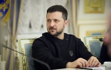 Президент Украины Владимир Зеленский за столом переговоров в черной толстовке с тризубом, обсуждающий соглашение Drone Deal с США.