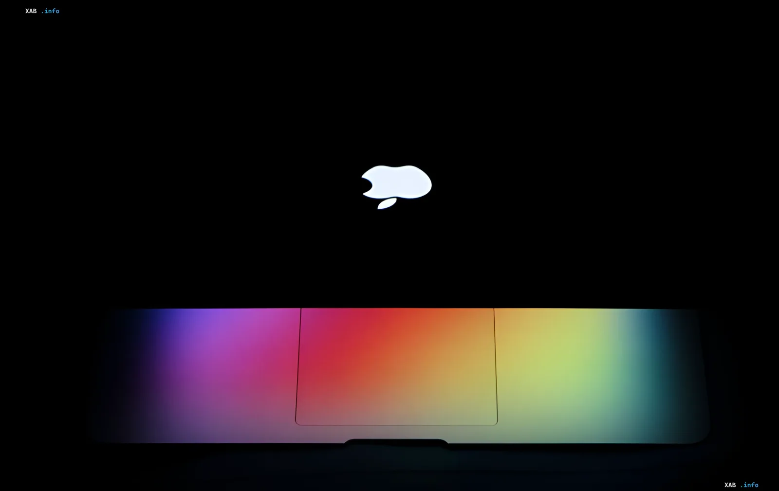 Логотип Apple на черном фоне с радужным градиентом на клавиатуре MacBook, символизирующий инновации в OLED-экранах и чипах M7