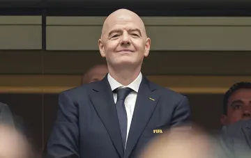 Жан-Мари Лефевр, президент ФИФА, в костюме с логотипом FIFA на фоне официального мероприятия, связанный со скандалом с Балогоуном и давлением от Трампа