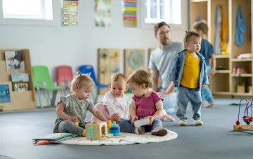 Діти граються у сучасному світлому приміщенні дитячого садка, що ілюструє нові стандарти безпеки та комфорту, які будуть впроваджені у будівництві дитячих закладів в Україні з 1 жовтня 2026 року.