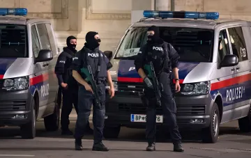 Вооруженные сотрудники австрийской полиции (Polizei) в масках и бронежилетах стоят у полицейских фургонов перед зданием, где находится полицейский участок в доме Гитлера, символизируя превращение нацистского символа в барьер для радикалов.