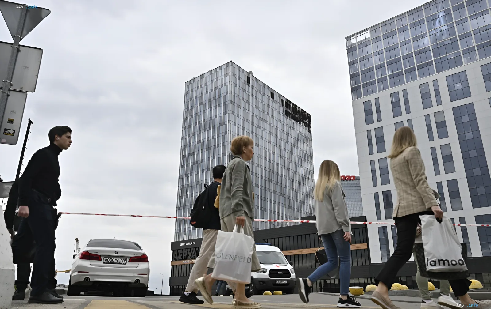 Люди с сумками проходят мимо здания в современном городе, иллюстрируя тему оттока населения и поиска новых возможностей за границей
