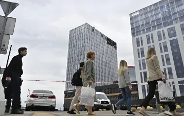 Люди с сумками проходят мимо здания в современном городе, иллюстрируя тему оттока населения и поиска новых возможностей за границей
