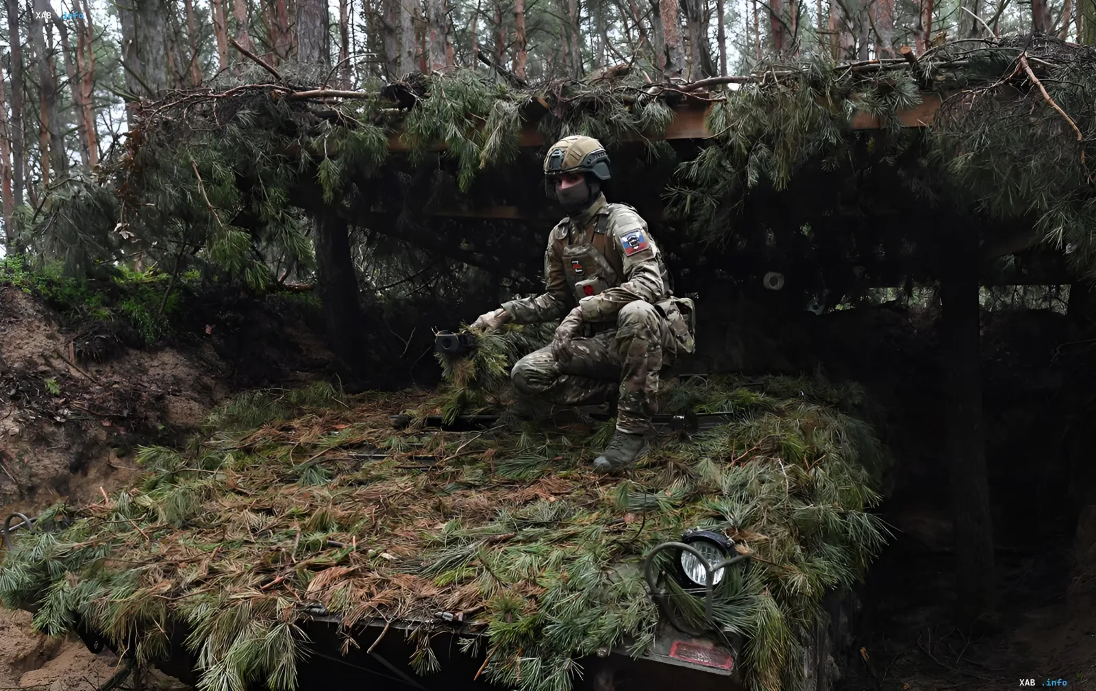 Российский военнослужащий в камуфляже и защитном шлеме, маскирующийся под еловыми ветками в лесу Харьковской области