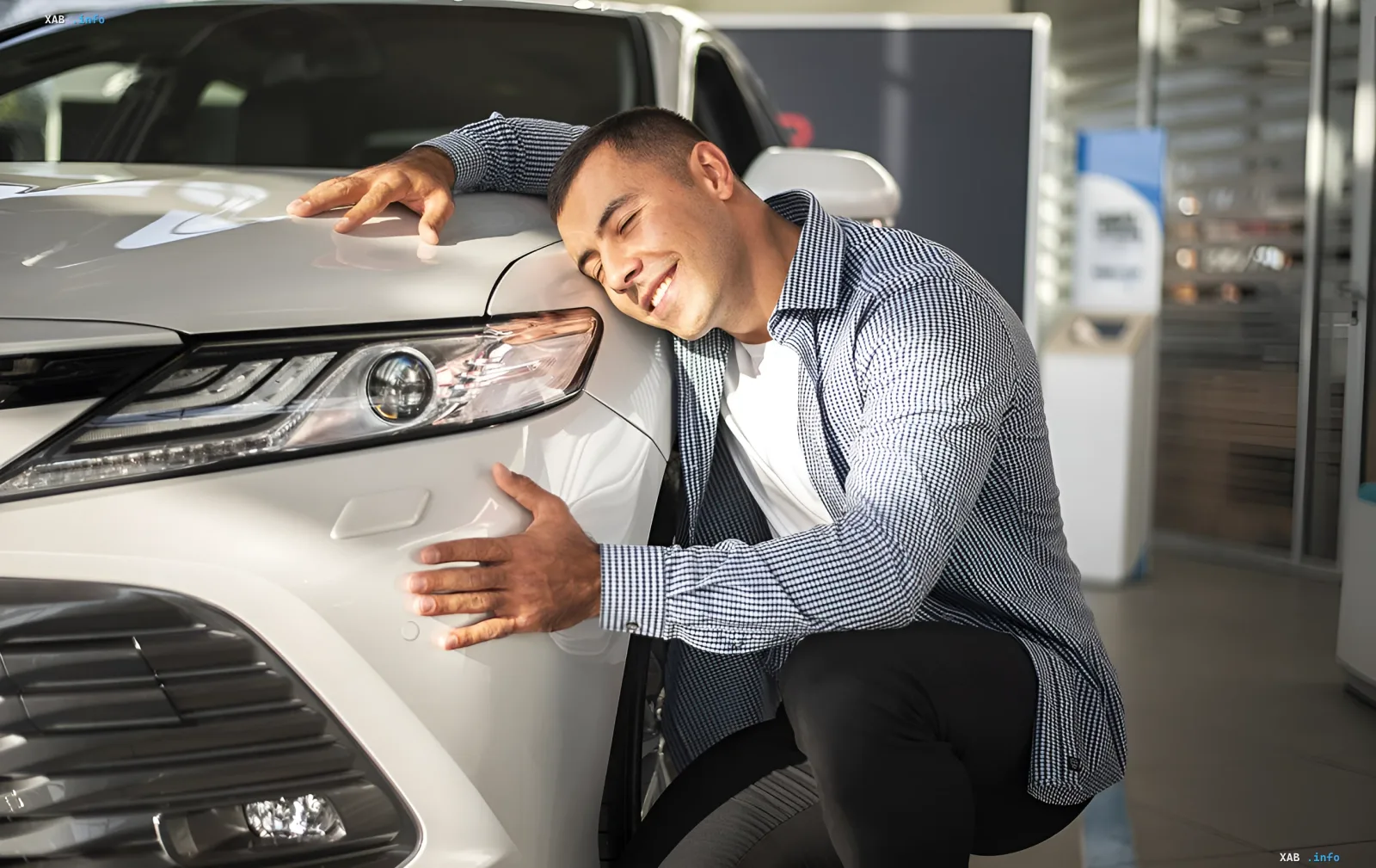 Glücklicher Mann umarmt ein weißes Auto im Showroom, was die wachsende Nachfrage nach Benzin- und Hybridfahrzeugen in der Ukraine symbolisiert