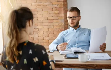Ernsthafter Interviewer mit Dokumenten diskutiert eine Stellenanzeige mit einem Kandidaten und illustriert das Paradoxon des ukrainischen Arbeitsmarktes im Jahr 2026