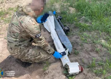 Сотрудник СБУ в камуфляжной форме осматривает обломки российского дрона-камикадзе, упавшего в приграничной зоне Украины