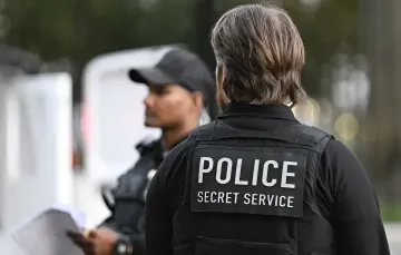 Agent der US-Secret Service in taktischer Weste mit Aufschrift 'POLICE SECRET SERVICE' während verstärkter Sicherheitsvorbereitungen für ein Trump-Veranstaltung
