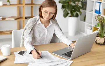 Frau mit Brille arbeitet am Laptop und füllt Dokumente aus – Illustration zum Artikel über Gehälter in der Ukraine und Arbeitskräftemangel