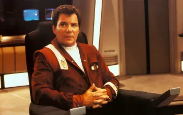 William Shatner als Captain James T. Kirk aus Star Trek, sitzend im Captain-Stuhl — Symbol seiner legendären Rolle und persönlichen Überwindung von Krebs
