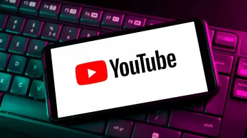 Логотип YouTube на экране смартфона, лежащего на клавиатуре с неоновой подсветкой — символ изменений в монетизации для AI-контента