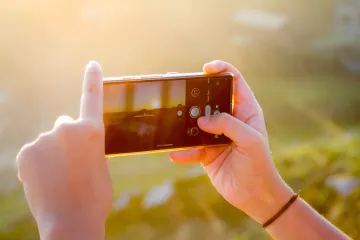 Person fotografiert Sonnenuntergang mit Smartphone-Kamera mit KI, zeigt Evolution vom einfachen Telefon zum intelligenten Fotografen