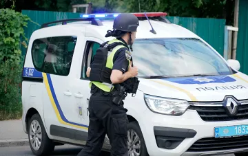 Поліцейський у захисному спорядженні стоїть біля патрульного автомобіля, забезпечуючи безпеку на блокпосту в Чернігові
