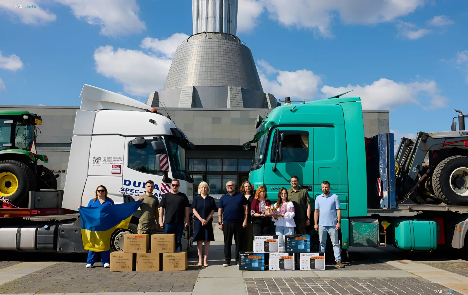 Gruppe von Freiwilligen mit ukrainischer Flagge und humanitärer Hilfe vor Lastwagen mit finnischer Technik vor einem Gebäude in Isjum