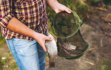 Fisherman holding a caught fish and a net with catch, illustrating fishing regulations and fines in Ukraine