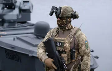 Боец СБУ в камуфляже с оружием и биноклем на фоне военного катера SeaBaby, участвовавшего в ударах по объектам в России