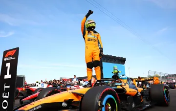 Ландо Норрис празднует победу на Гран-При Венгрии, стоя на болиде McLaren с поднятой рукой